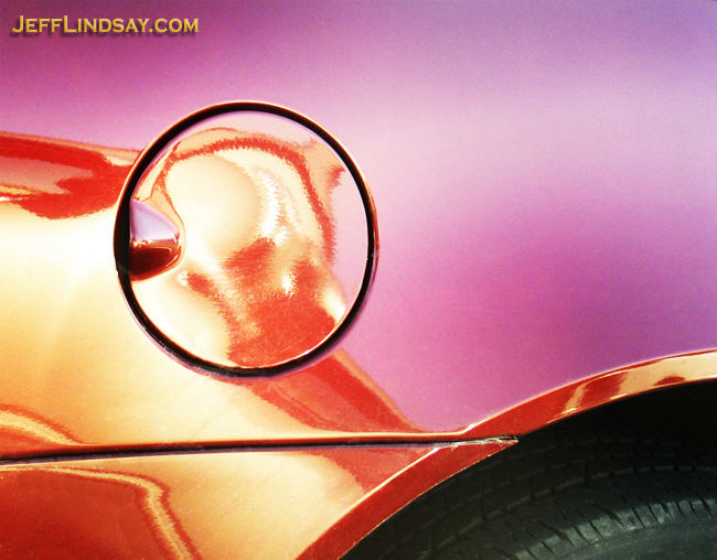 A portion of an automobile. As I was getting into my car one afternoon in 2006  in a Kimberly-Clark parking lot in Neenah, Wisconsin, I noticed the shiny red car next to me and felt compelled to take a photo. I strengthened the coloration slightly and removed a couple of water spots.