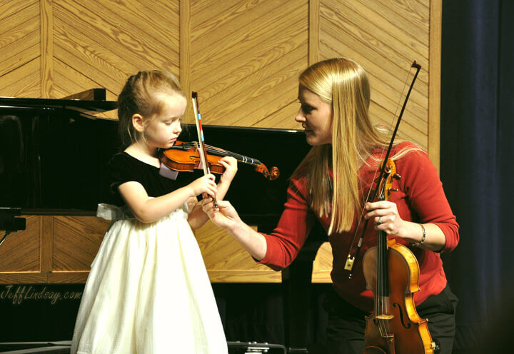 girl prepares to play her violin, gently guided by her excellent teacher.