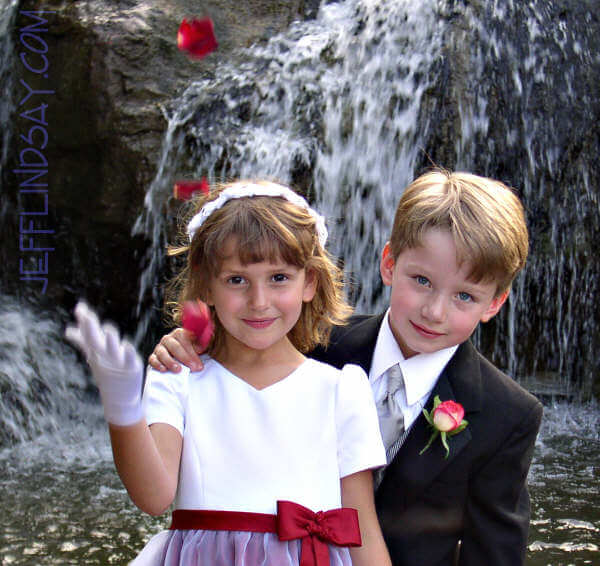 Two children as the flower girl tosses some rose petals.